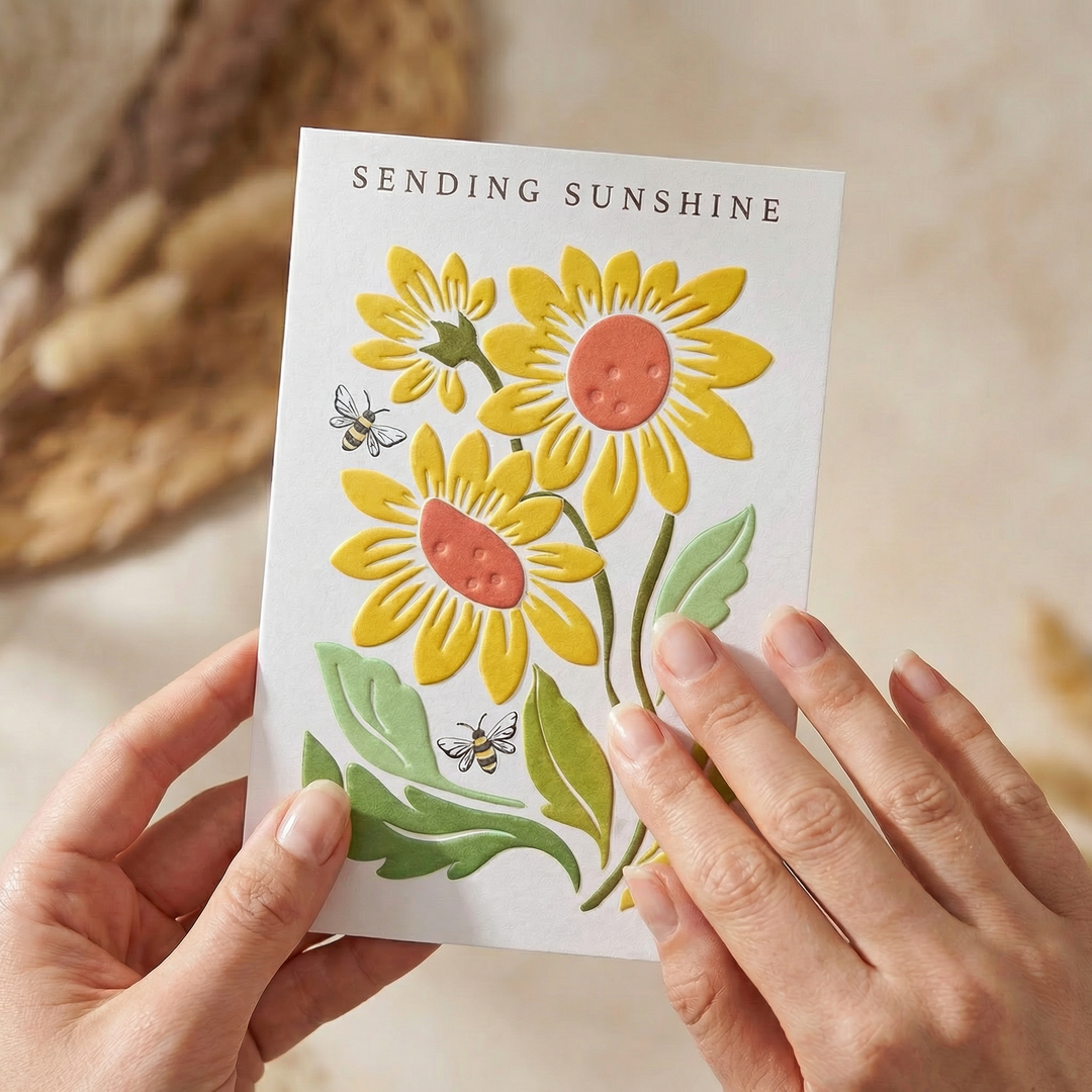 Card with sunflower design held by hands, text 'Sending Sunshine' on a blurred background