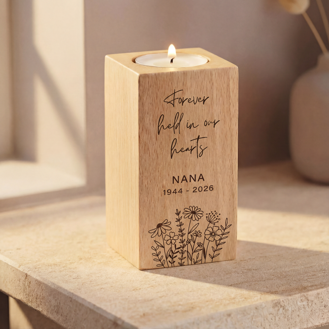 Wooden candle holder with engraved text and floral design on a surface.